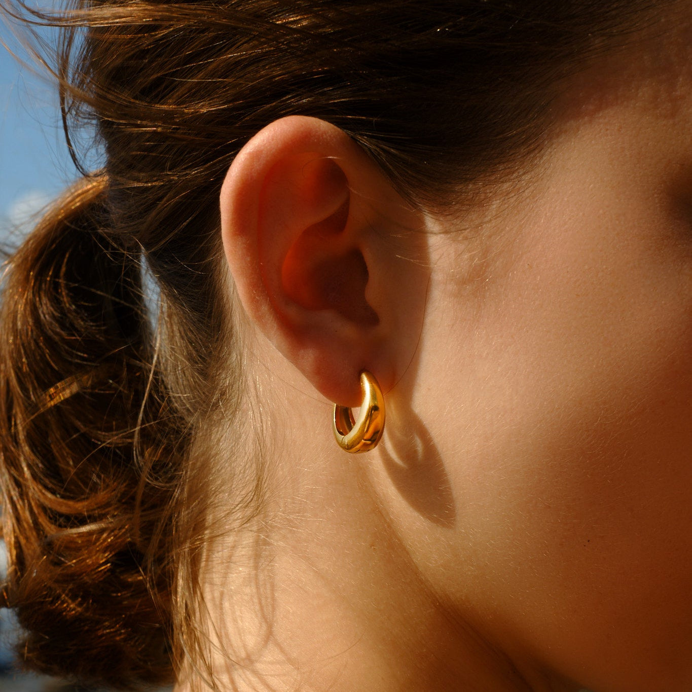 Close-up of a person wearing a gold hoop earring with a blurred background