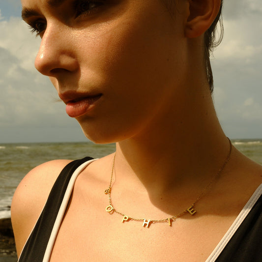 Woman wearing a gold name necklace with letters against a beach background
